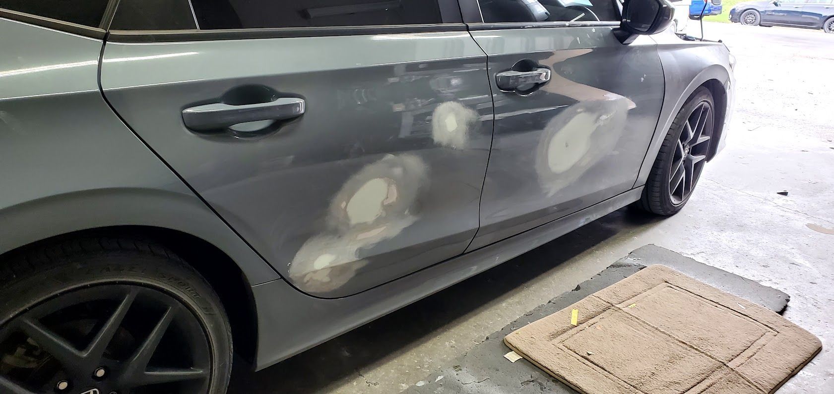 Silver sedan with several white paint scuffs on the side, parked on a wet driveway near a curb ramp