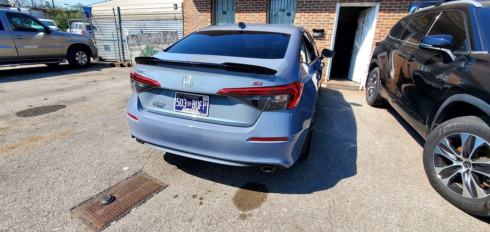 Silver sedan parked in a gravel lot beside black SUVs, rear view