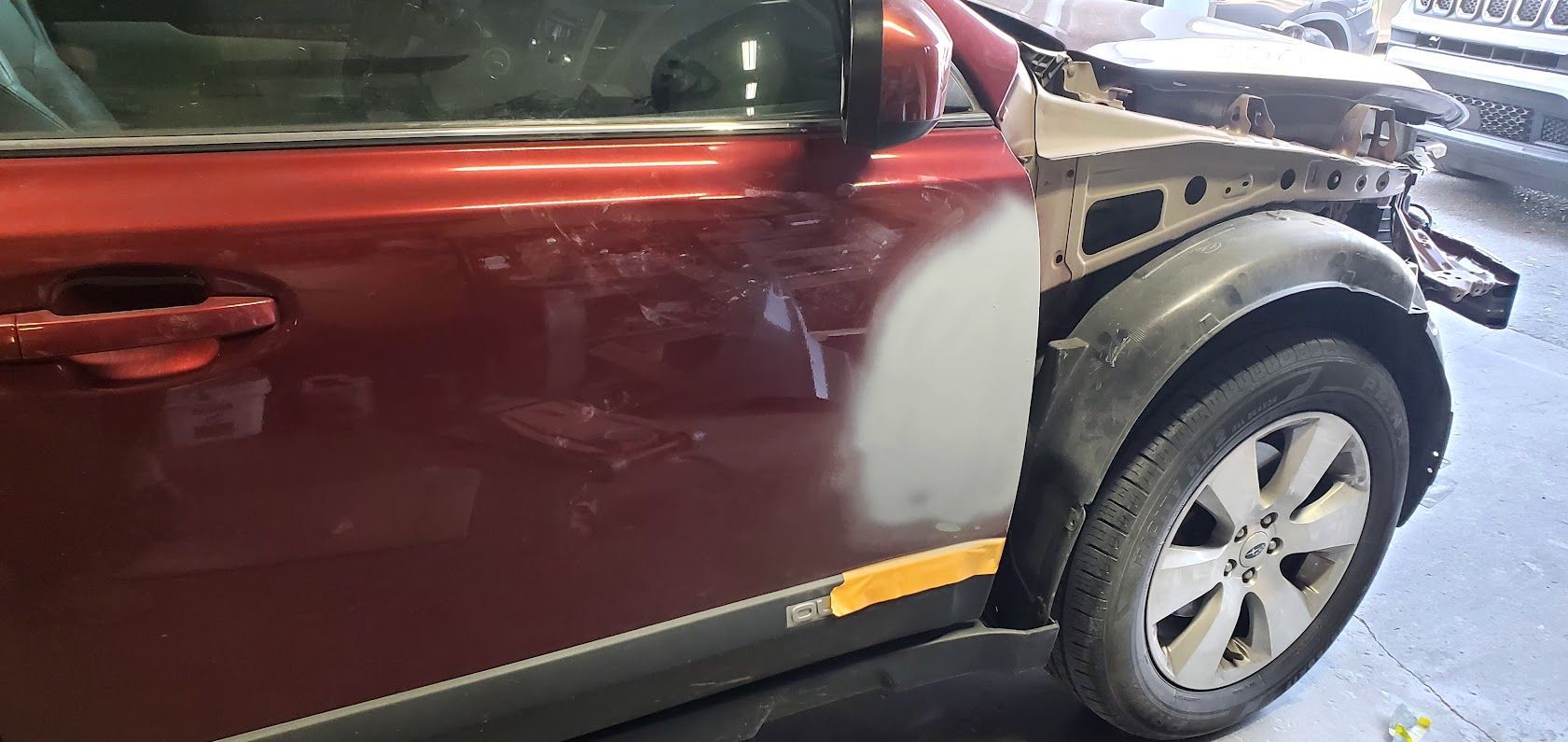 Maroon SUV with side damage and a dented front bumper in a garage