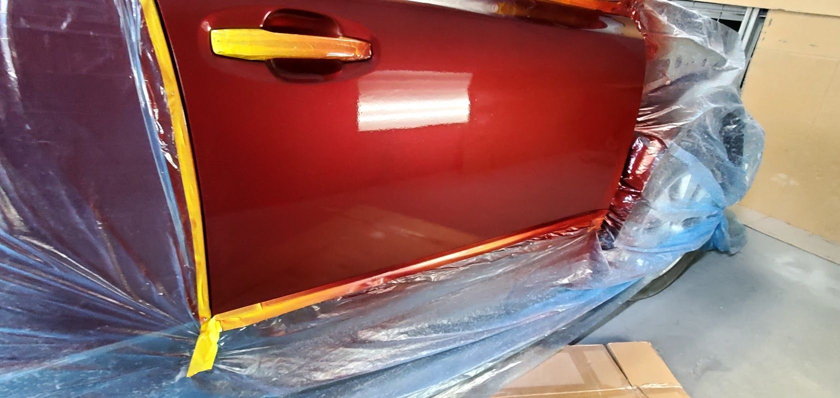 Red car door wrapped in protective plastic masking during painting or repair