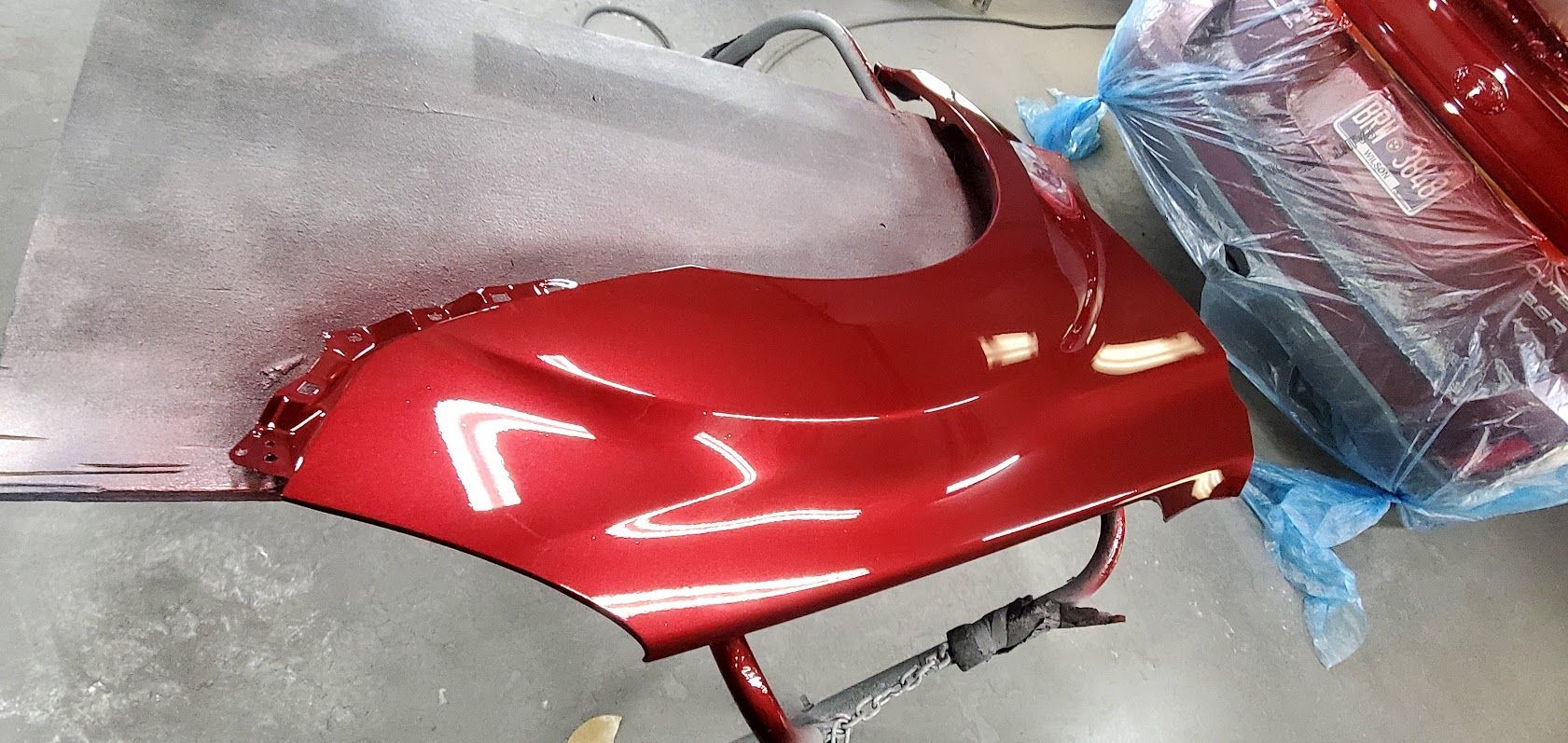 Red scooter fairing wrapped in glossy red vinyl on a workbench, with protective plastic nearby