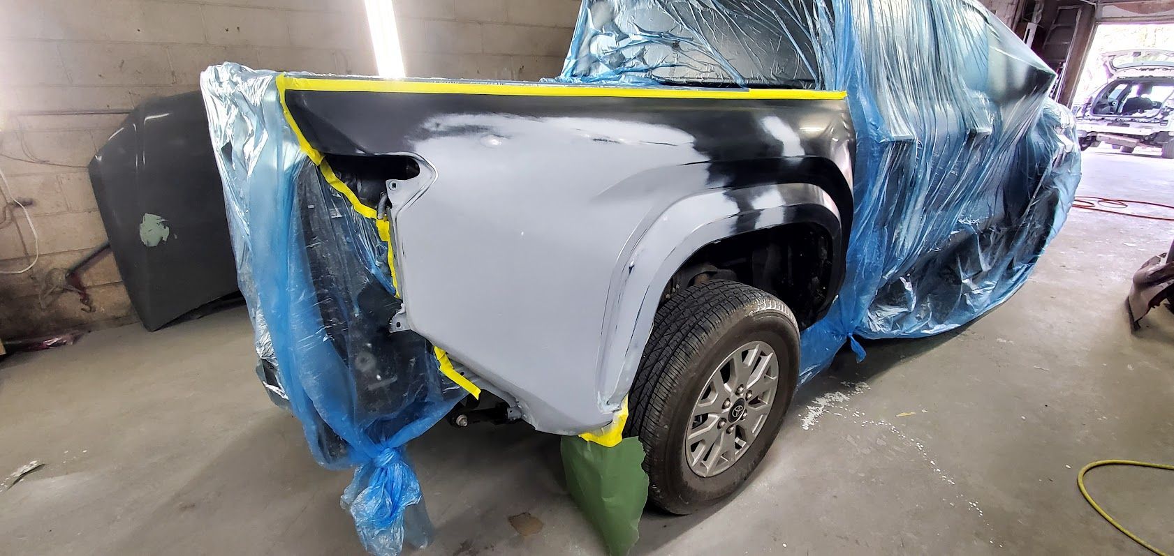 Damaged white car body wrapped in blue plastic in a repair shop, rear wheel exposed