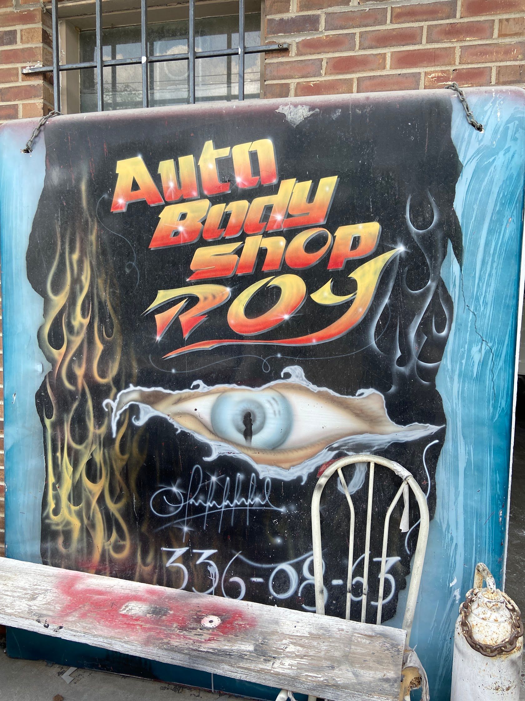 Colorful street mural reading “Auto Body Shop 709” with a single eye and teeth-like graphic on a brick wall