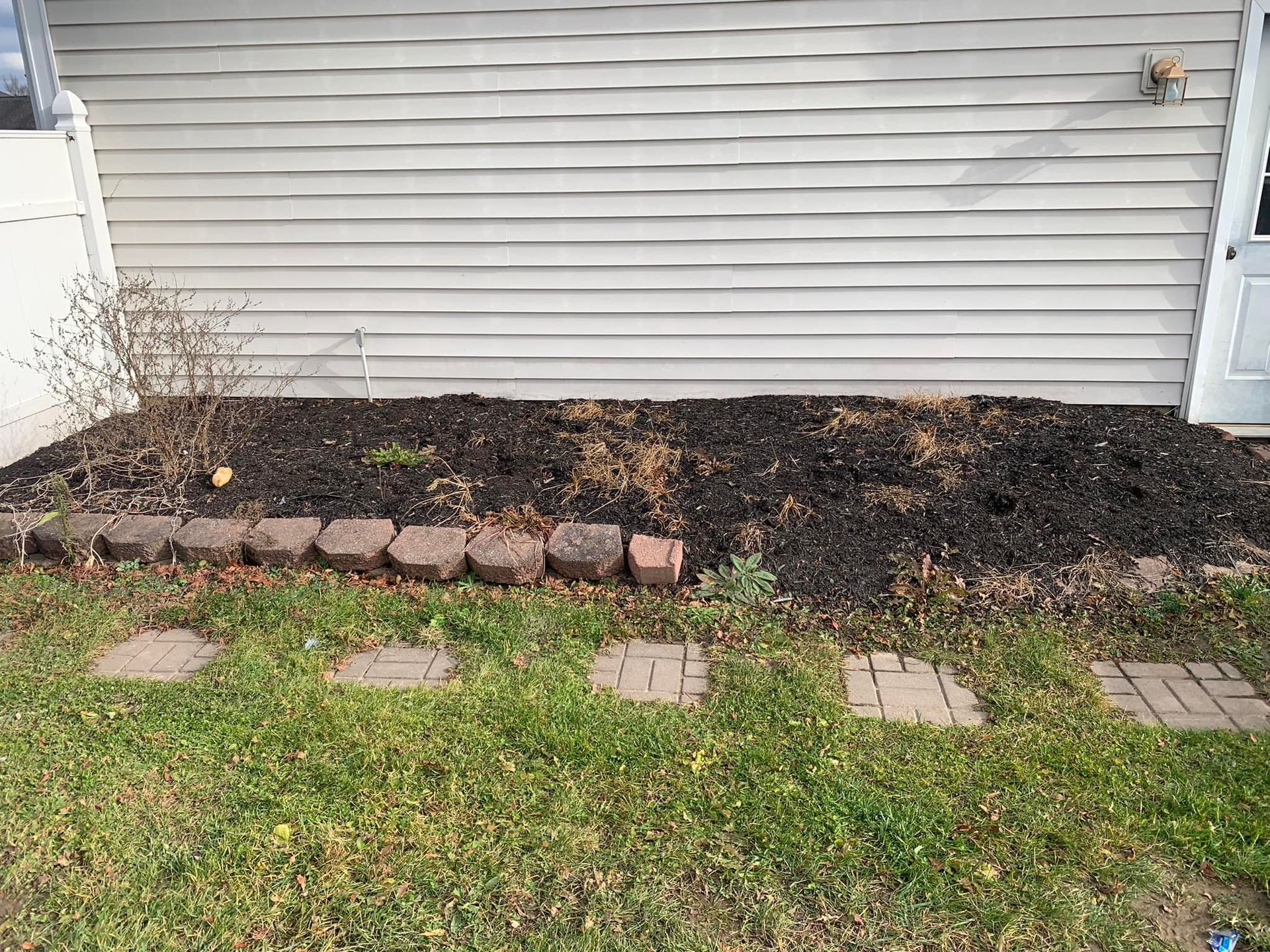 A backyard with a brick walkway and a pile of mulch in front of a house.