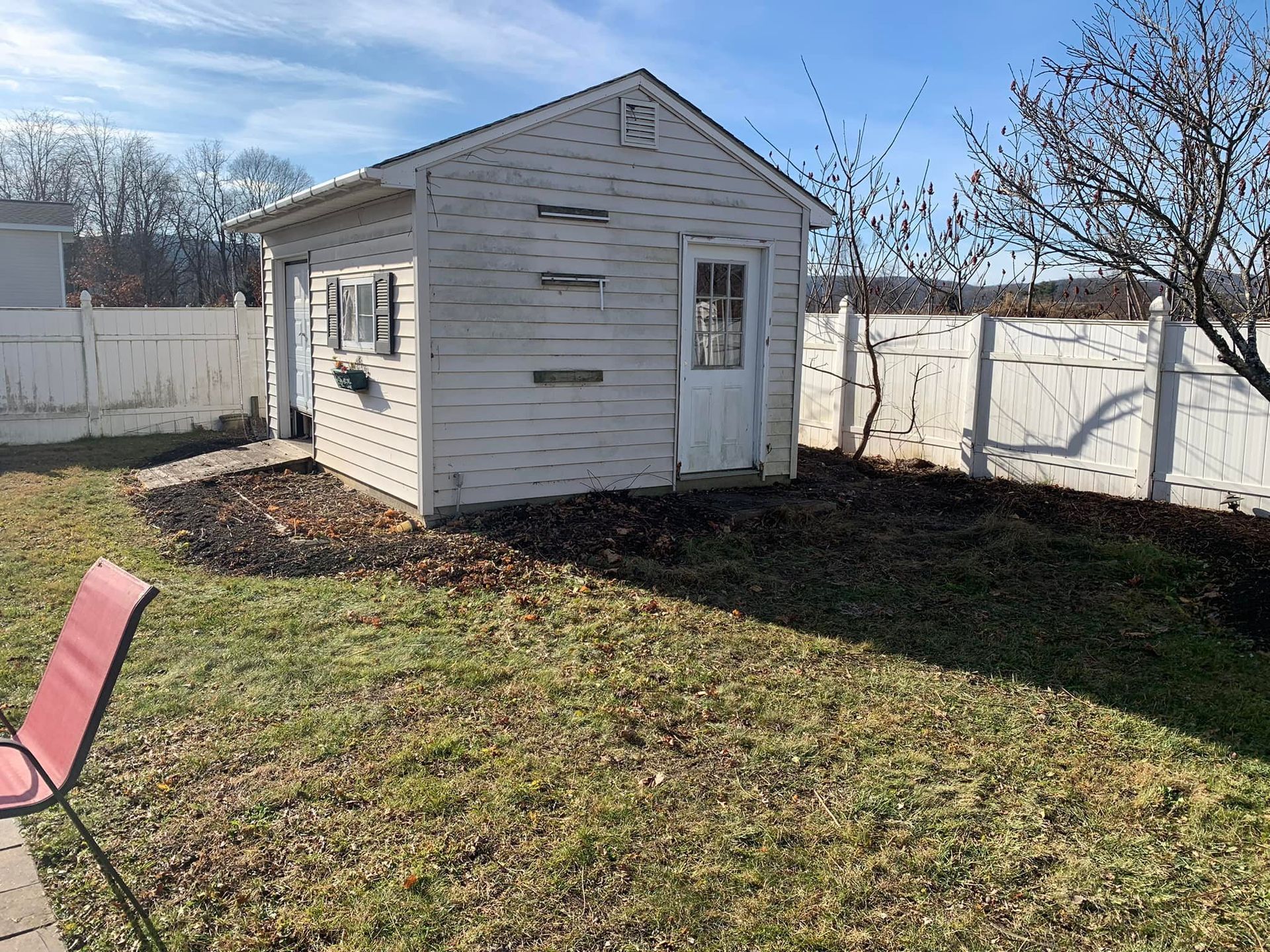 A small white shed is sitting in the middle of a grassy yard.