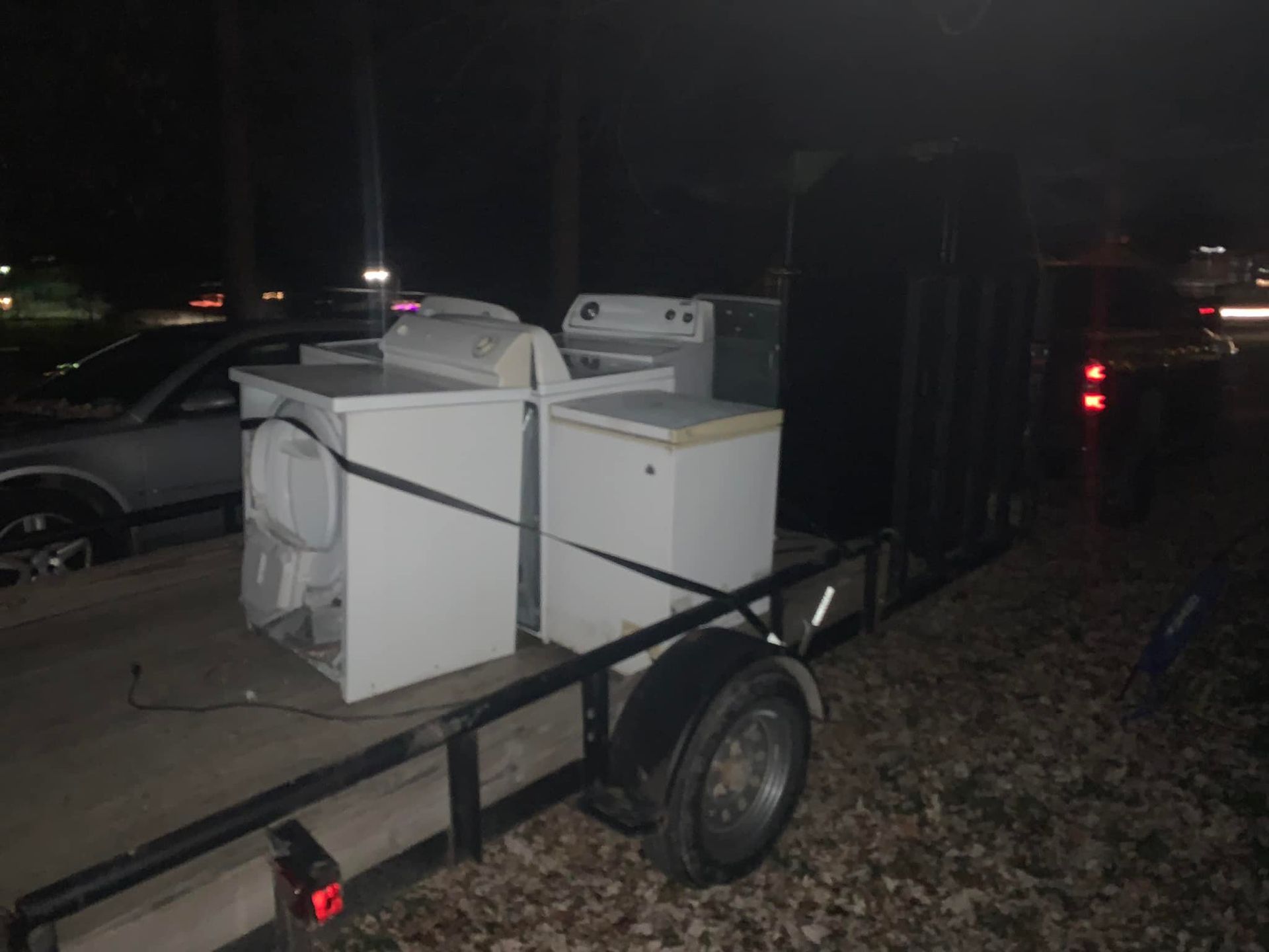 A trailer with a washer and dryer on it is parked in a dark parking lot.