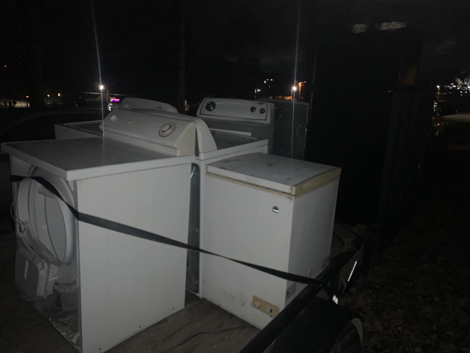 A washing machine , dryer , and freezer are tied together with a strap in the back of a truck.