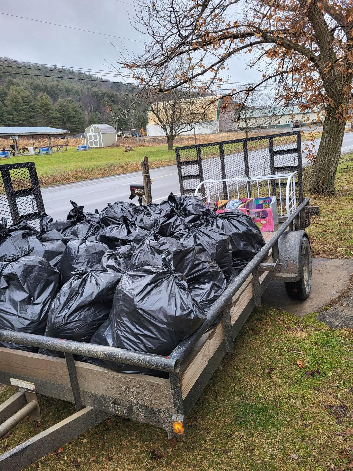 A trailer filled with bags of trash is parked in the grass.