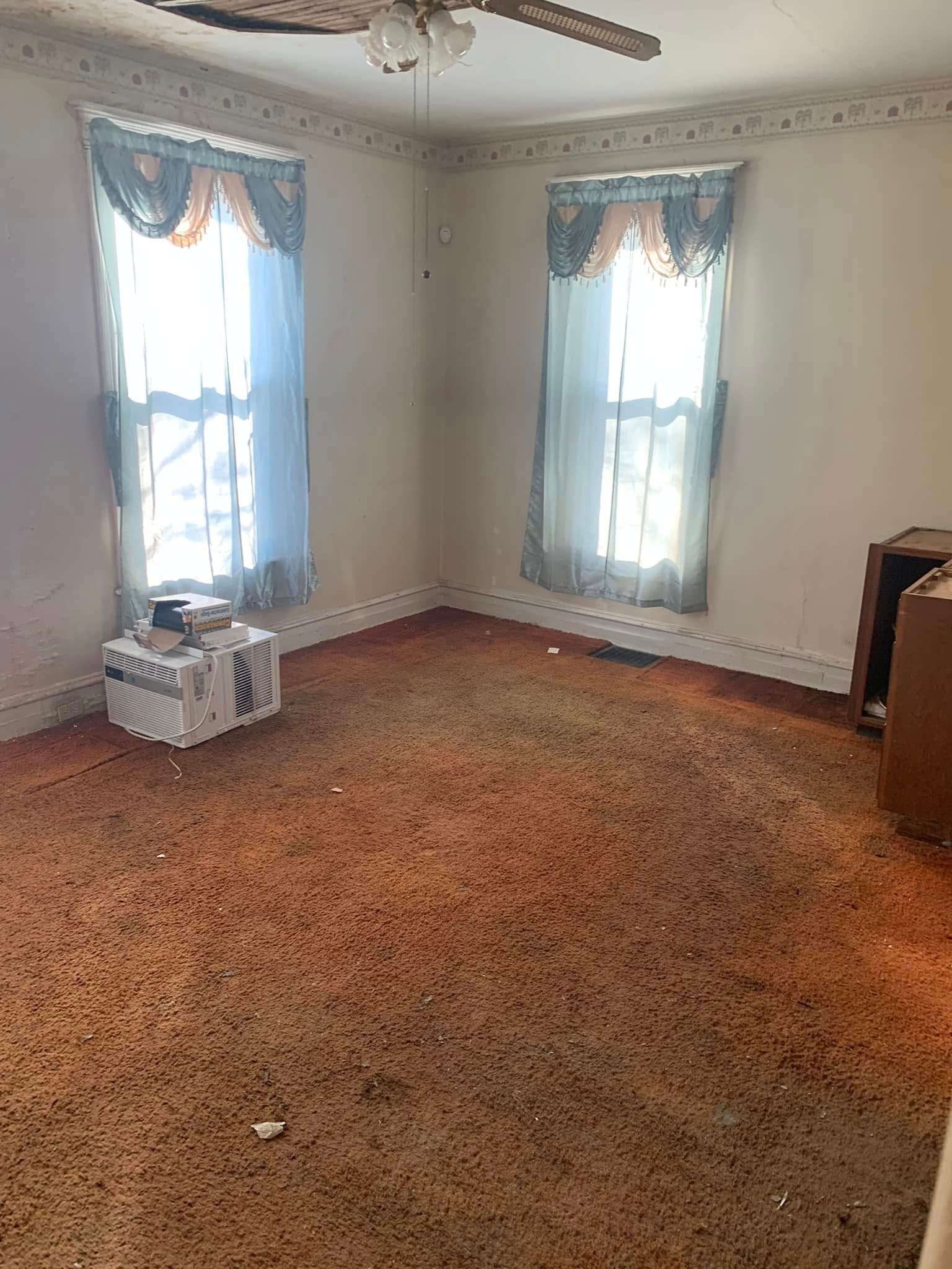 An empty living room with a ceiling fan and two windows.