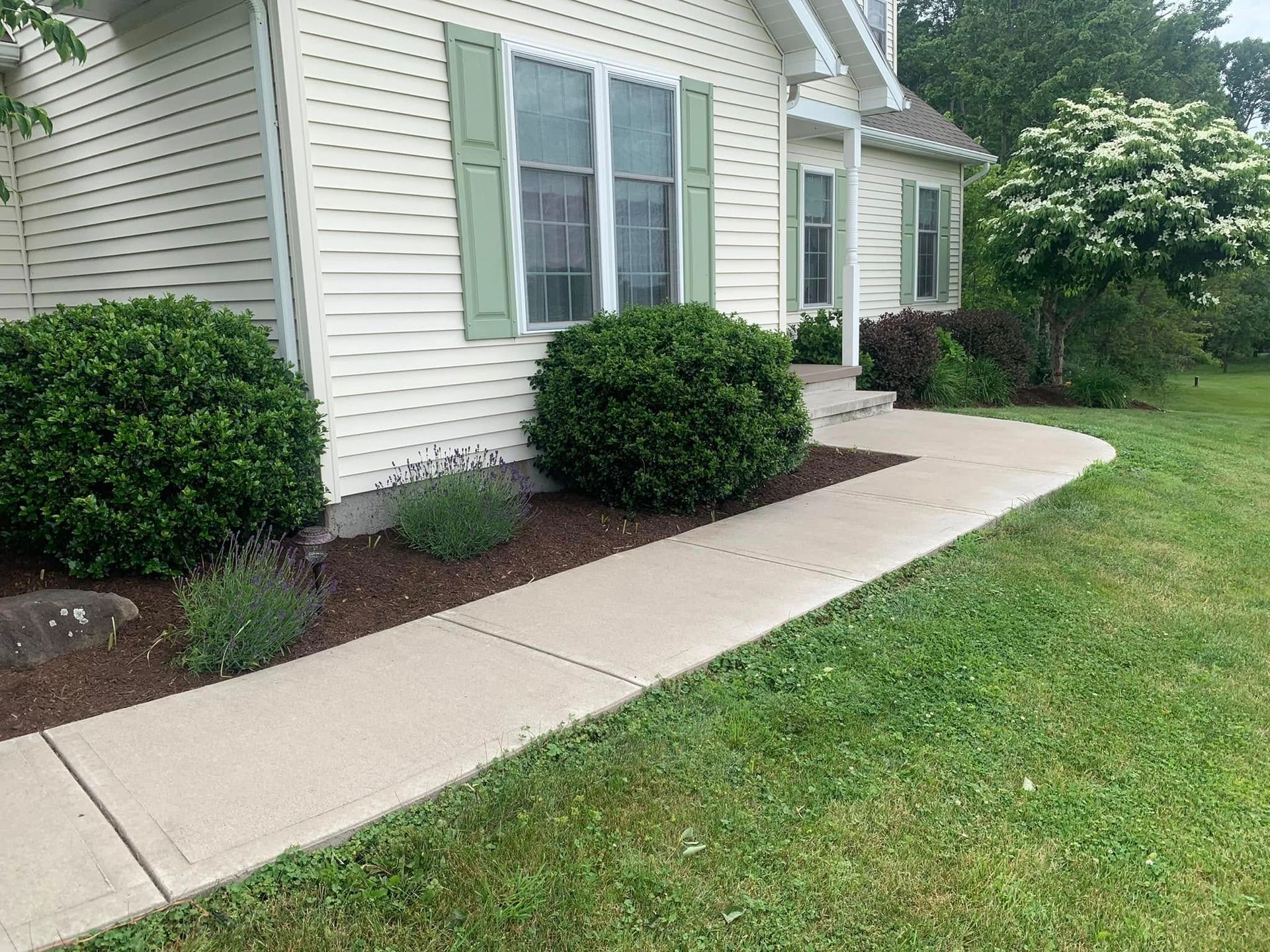 A white house with green shutters and a sidewalk in front of it.