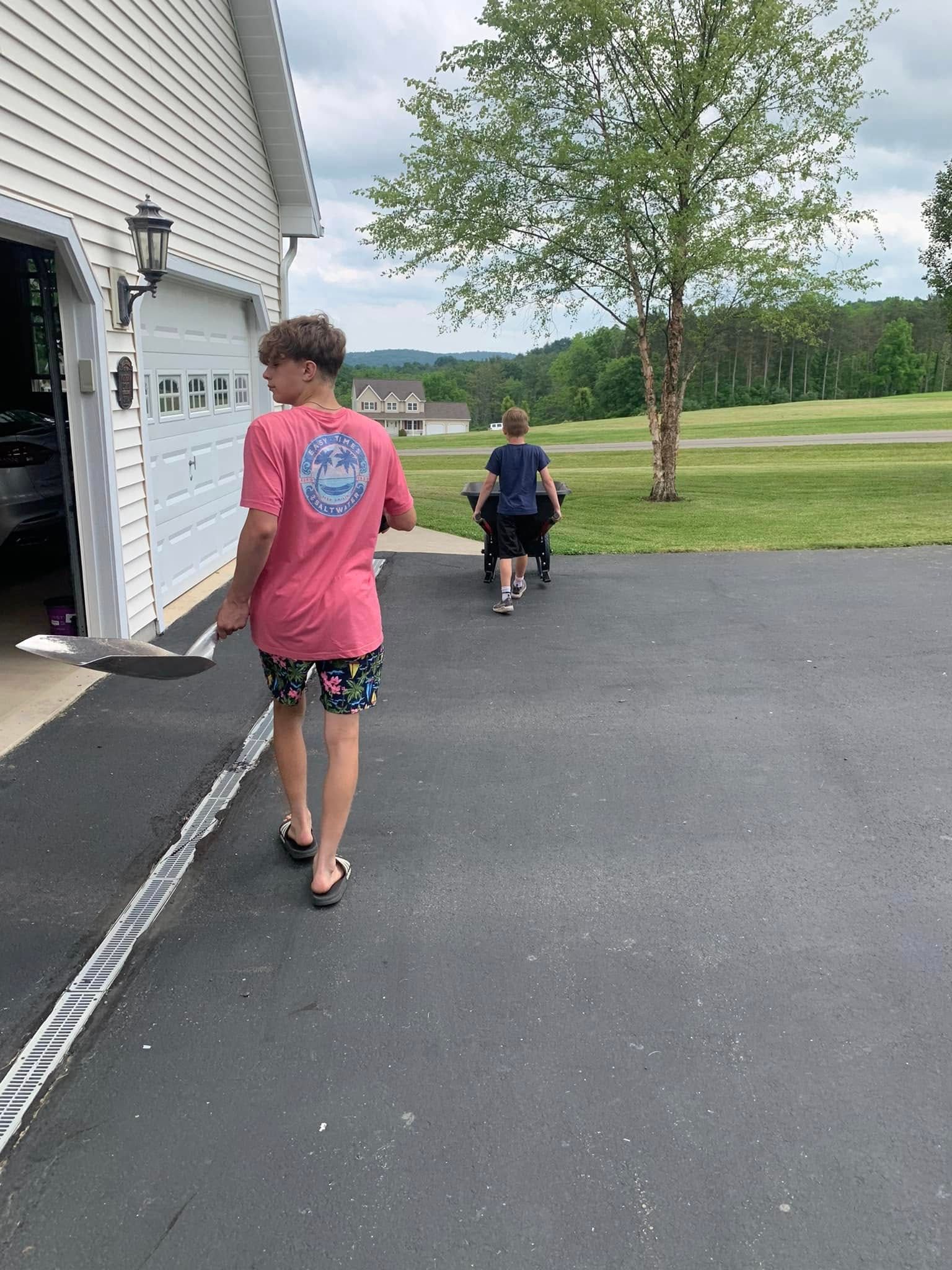 A man in a pink shirt is walking down a driveway with two children.
