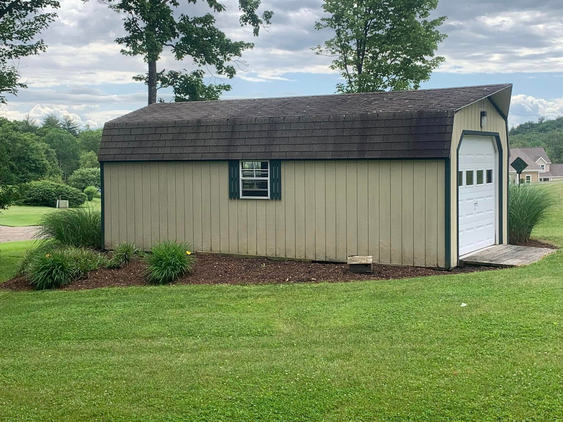 A shed with a garage door is sitting in the middle of a grassy field.