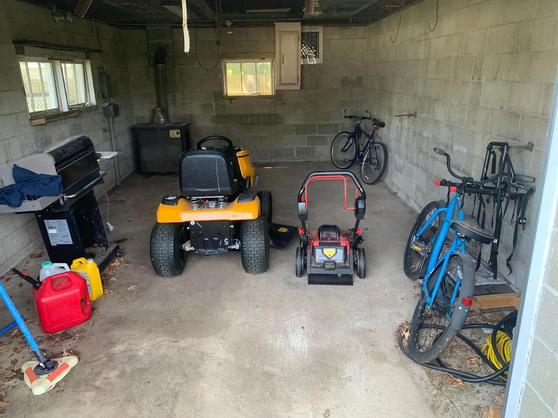 A garage with a lawn mower , bicycles , and a grill.