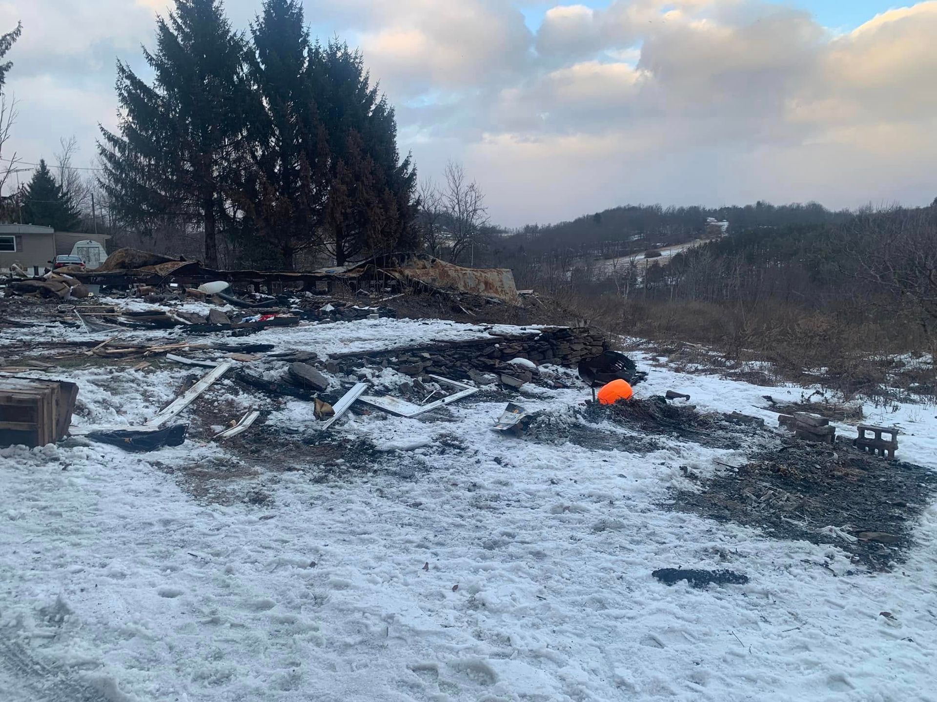 A snowy field with a pile of rubble and trees in the background.