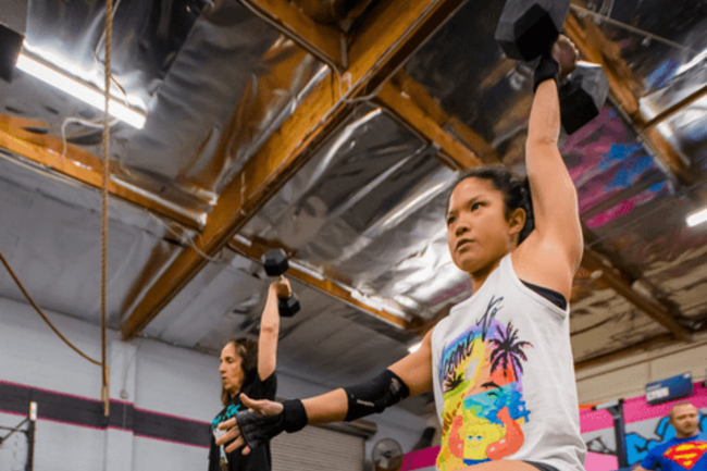 Two women are lifting dumbbells in a gym.