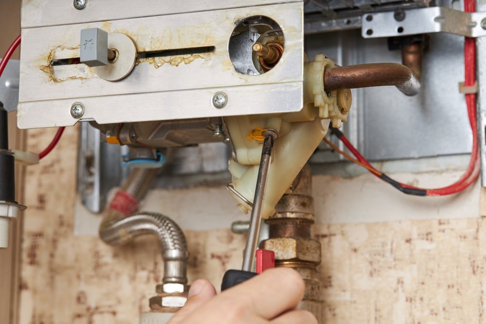 Person using a screwdriver to repair a gas boiler, close-up.