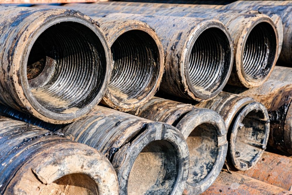 Stacked, dirty metal pipes with threaded ends, possibly for oil drilling.