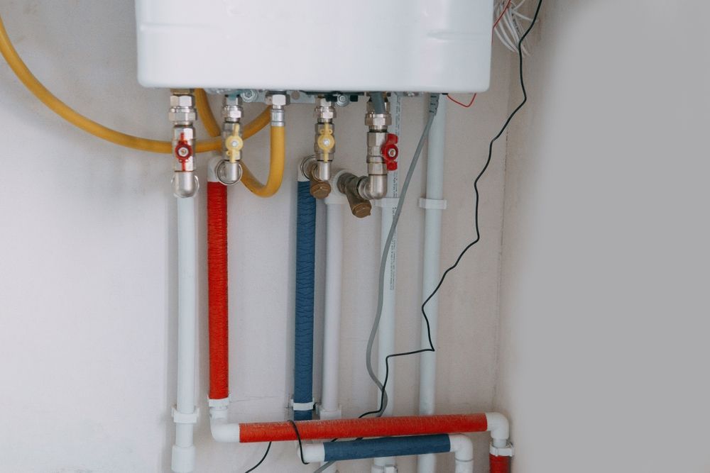 White water heater with red and blue pipes and valves against a white wall.