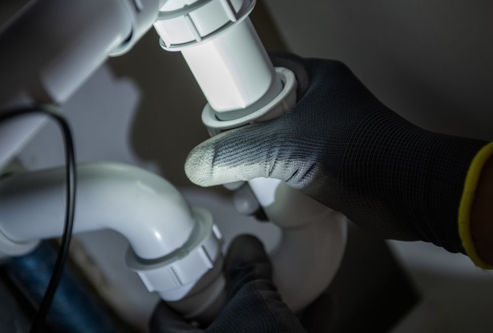 Gloved hands connecting white plumbing pipes under a sink.
