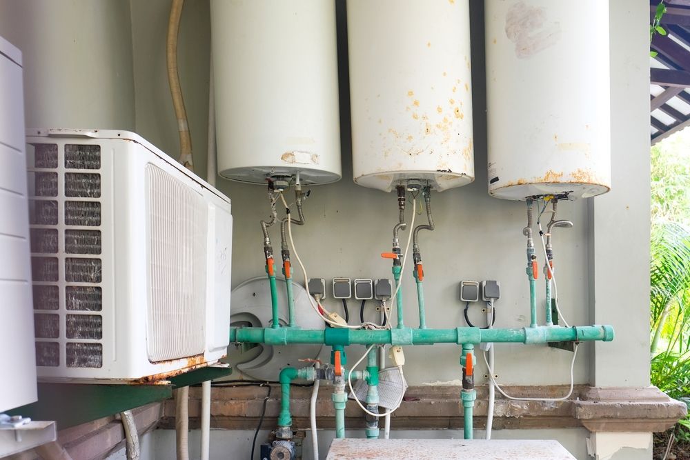 Air conditioning unit, three water heaters, and associated green piping mounted on a wall.