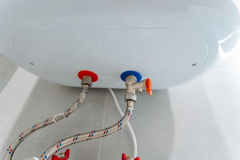 White water heater with red and blue water line connections, mounted on a tiled wall.