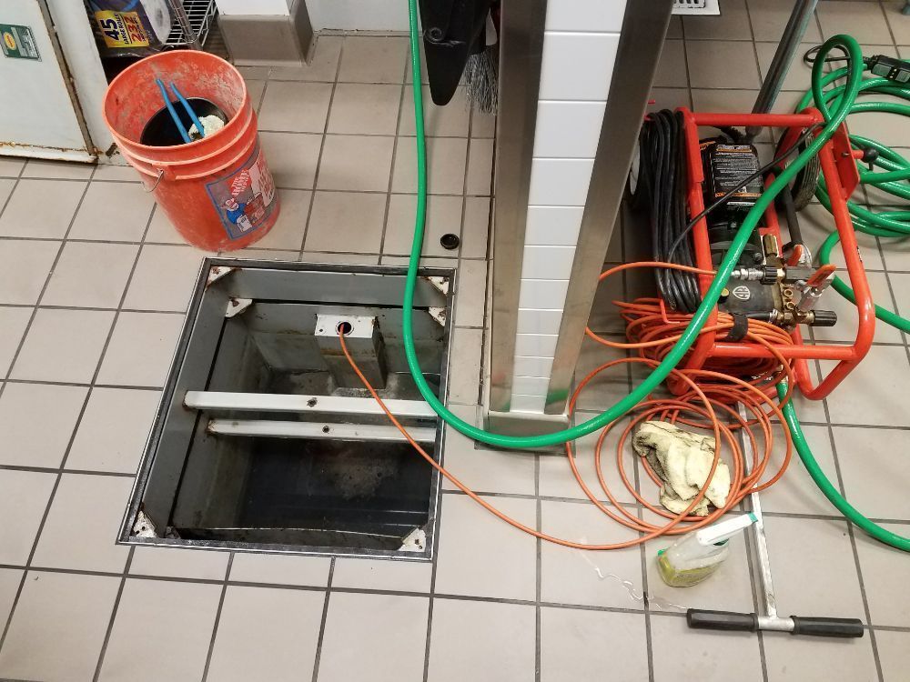 Open floor drain next to a stainless steel structure; cleaning equipment and bucket nearby.