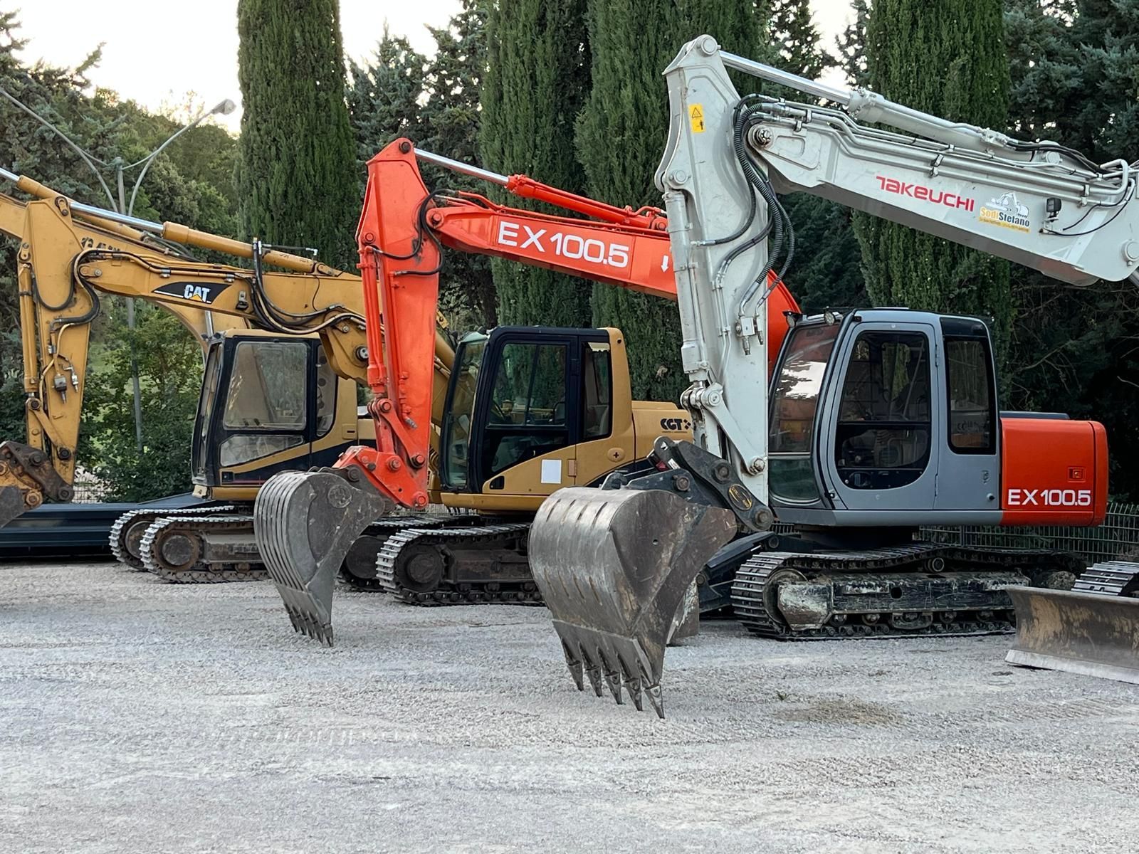 Una fila di escavatori è parcheggiata in un piazzale ghiaioso.