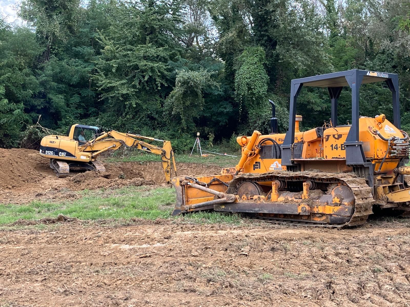 Un bulldozer e un escavatore sono parcheggiati in un campo sterrato.