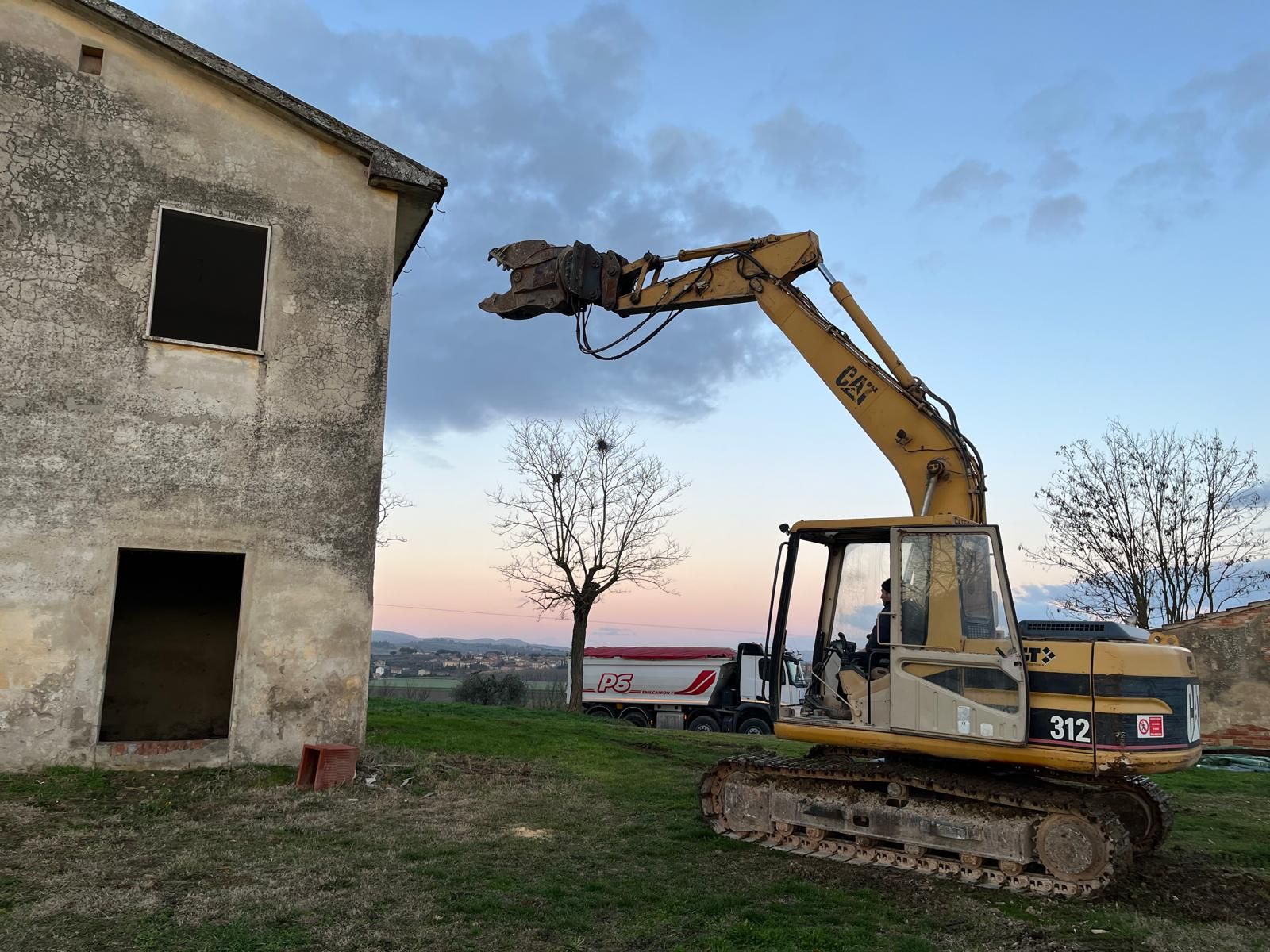 Un escavatore giallo è in piedi davanti a un vecchio edificio