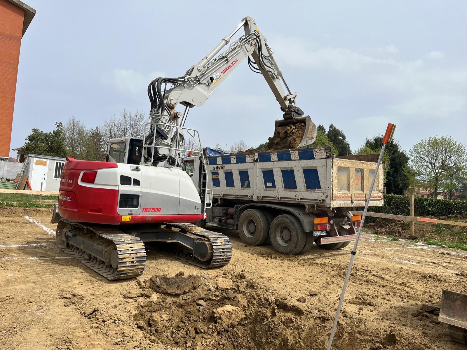 Un escavatore rosso e bianco sta caricando terra su un autocarro con cassone ribaltabile.