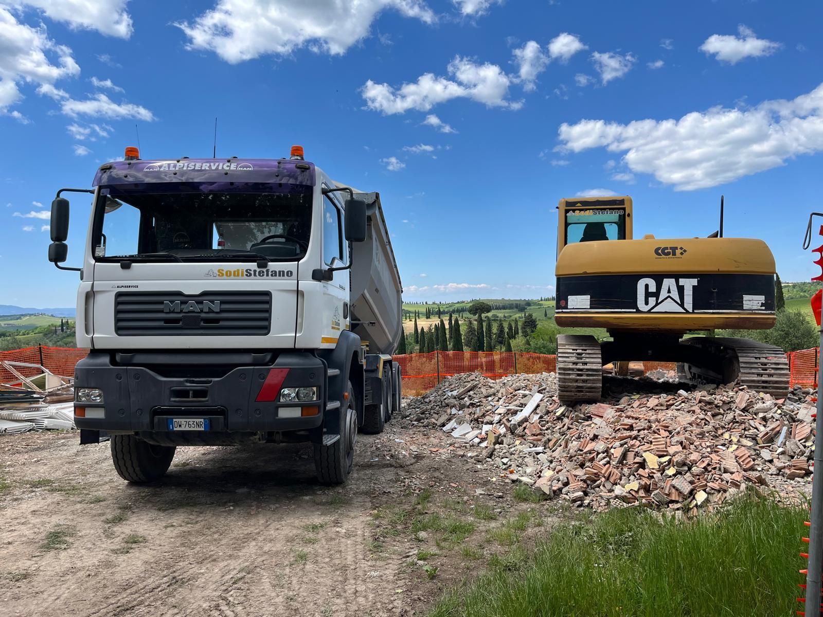Un autocarro con cassone ribaltabile e un escavatore Caterpillar sono parcheggiati uno accanto all'altro su una strada sterrata.