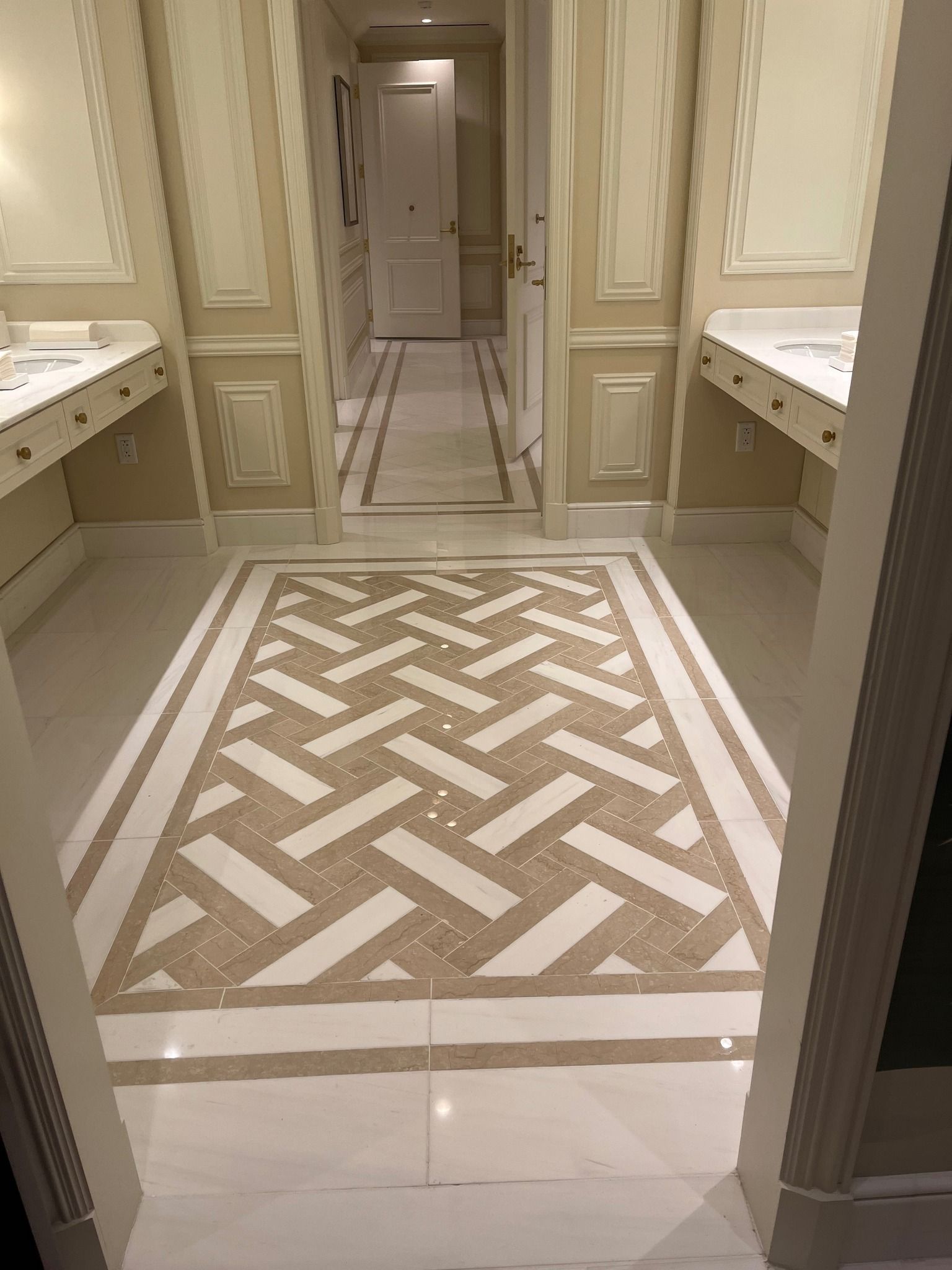 Elegant beige restroom with patterned marble floor, wall mirrors, and sinks on both sides