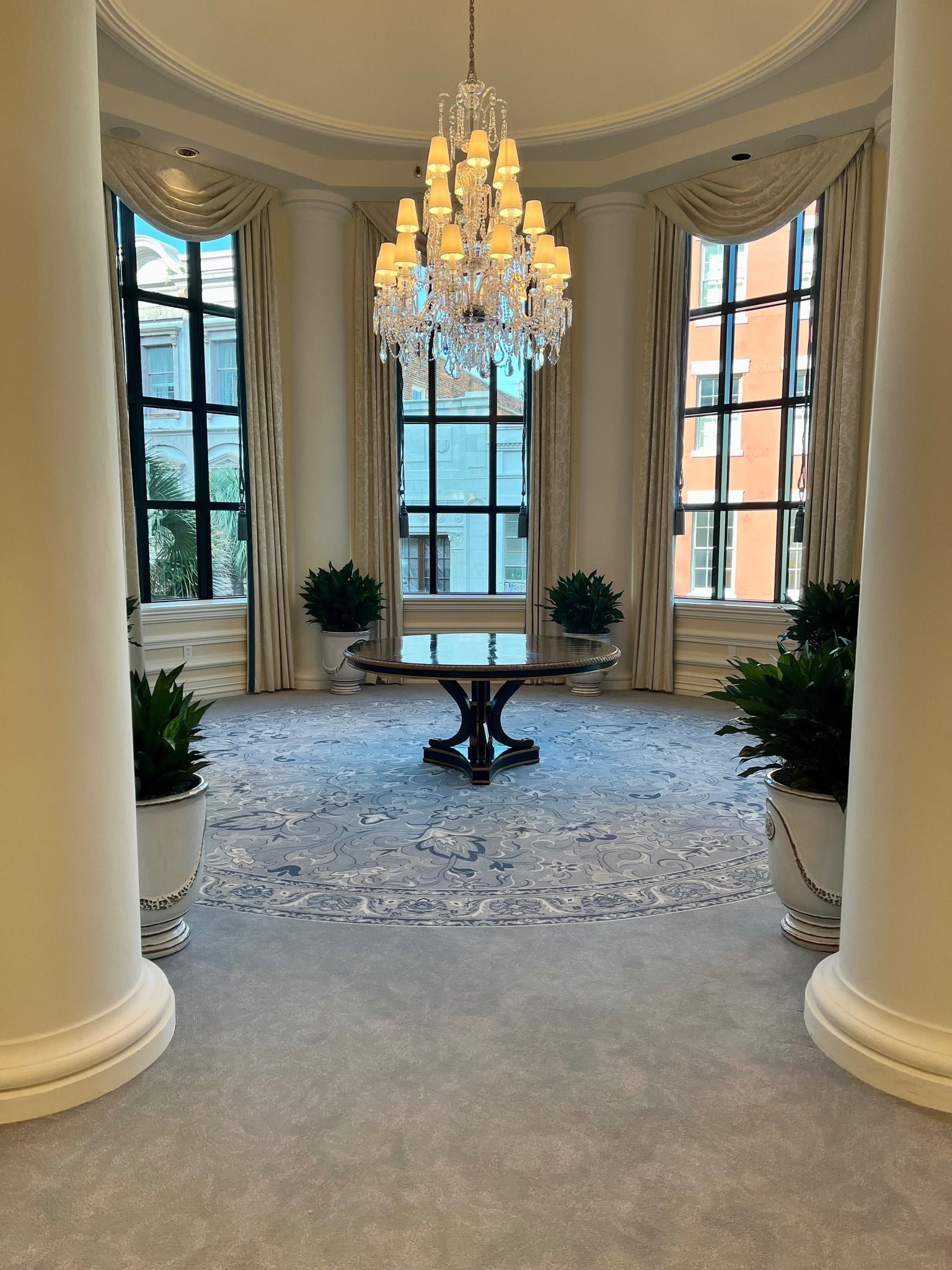 Elegant living room with chandelier, tall windows, round table, and blue patterned rug