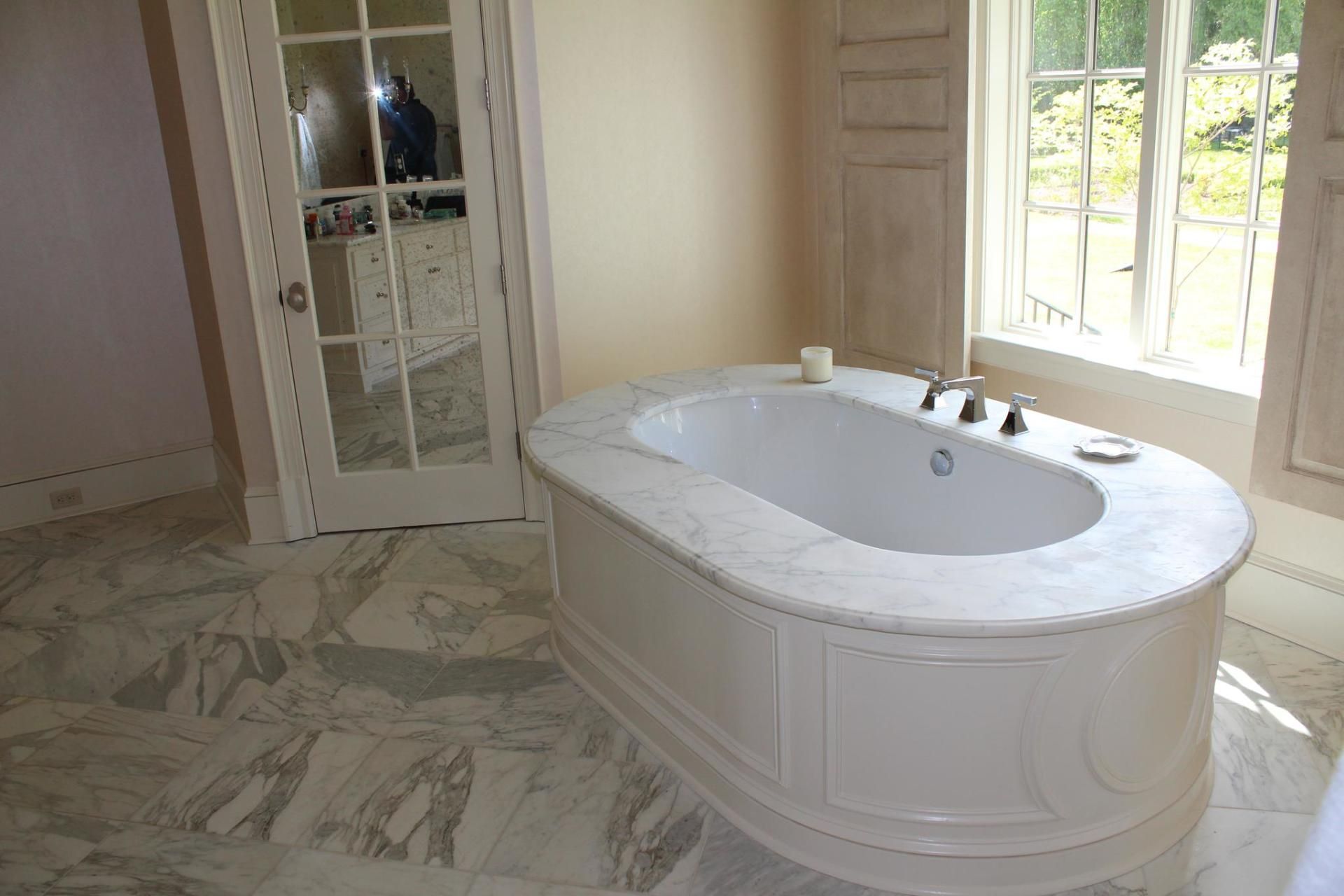 Luxurious bathroom with a white soaking tub, marble floor, and large windows with curtains