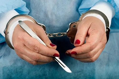 Hand of a surgeon with a scalpel in handcuffs.