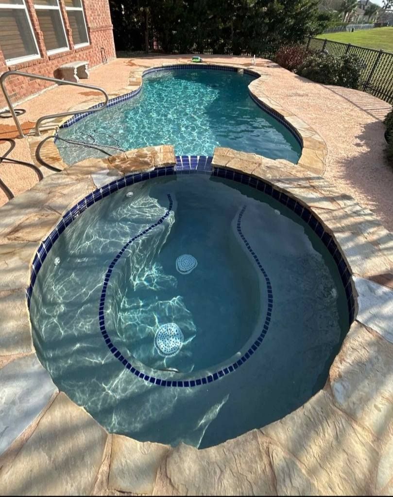 Swimming pool with an attached hot tub, both filled with water and surrounded by stone.