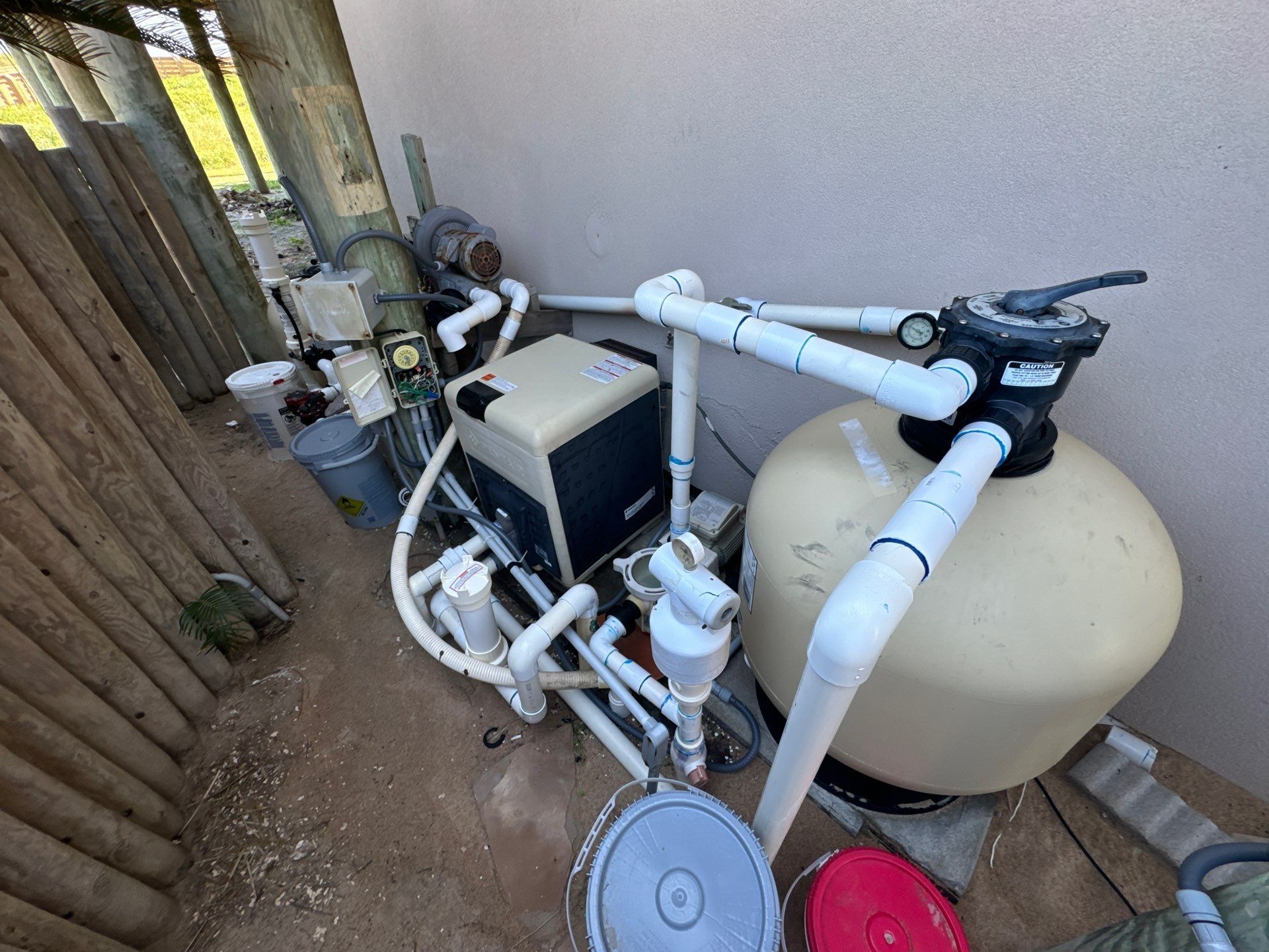 Pool equipment setup with a filter, heater, and pipes against a wall.