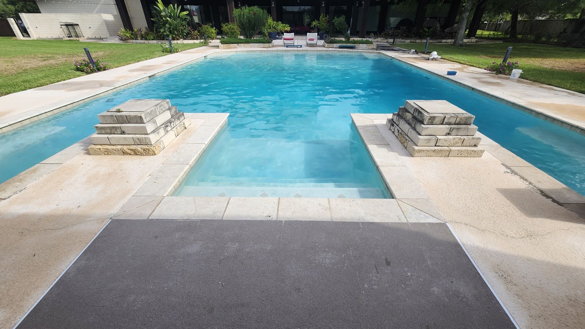 Swimming pool with concrete steps and two decorative stone pillars.