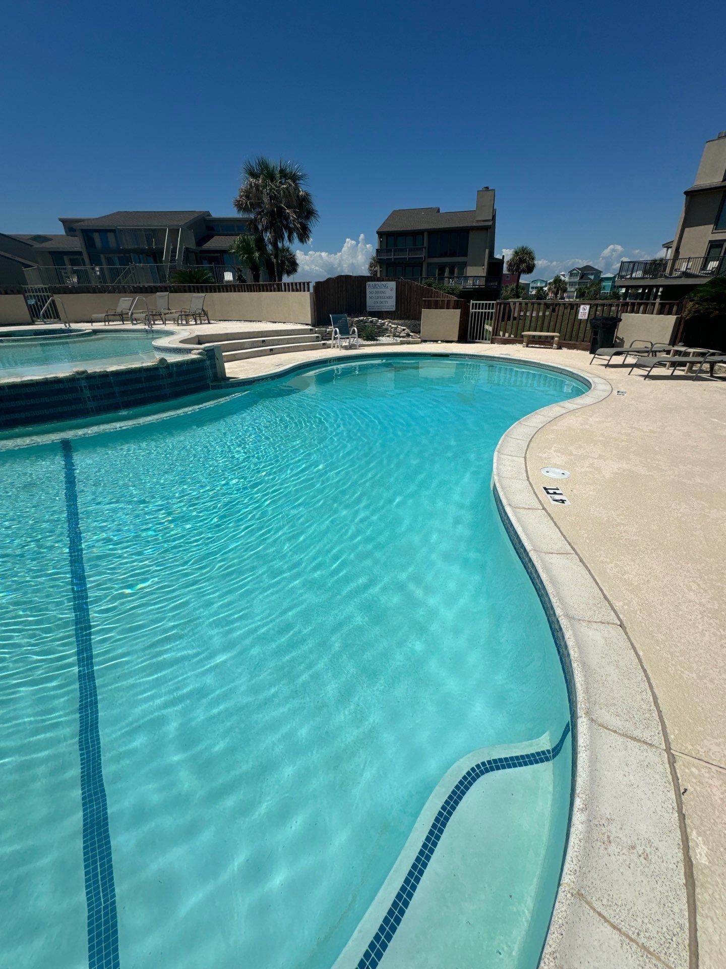 A clear blue swimming pool with buildings in the background under a bright blue sky.