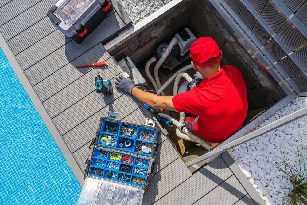 Pool technician repairs equipment in a pit beside a pool, tools and parts visible.