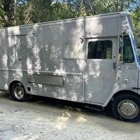 Gray food truck parked on a tree-lined dirt road, side view