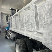 White dump truck inside a cargo hold or warehouse, viewed from the side with large wheels and bed visible