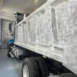 White dump truck inside a cargo hold or warehouse, viewed from the side with large wheels and bed visible