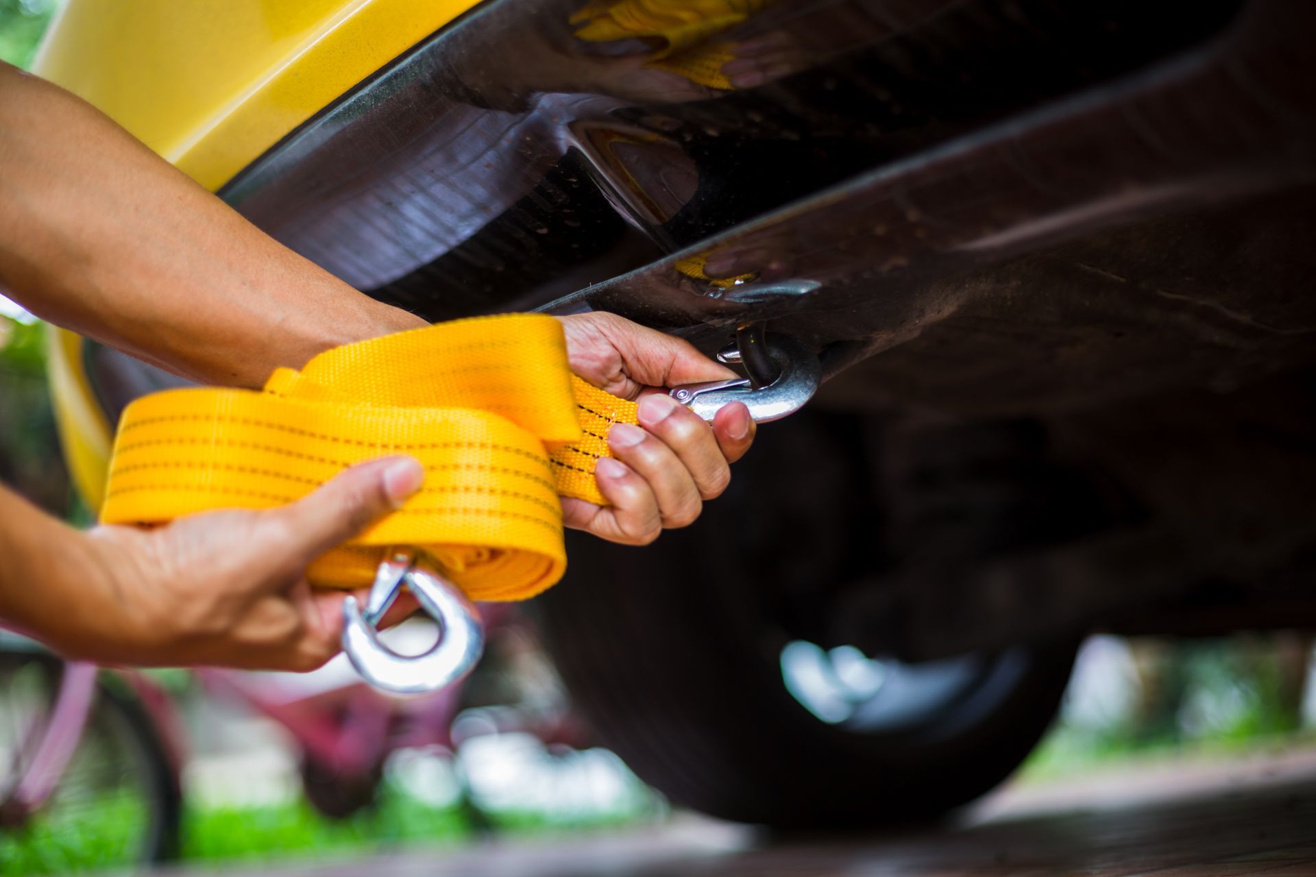 Hands attaching a yellow tow strap to a vehicle's undercarriage.