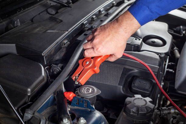 Jumper cables connected to a car battery in an engine compartment; red and black clamps.
