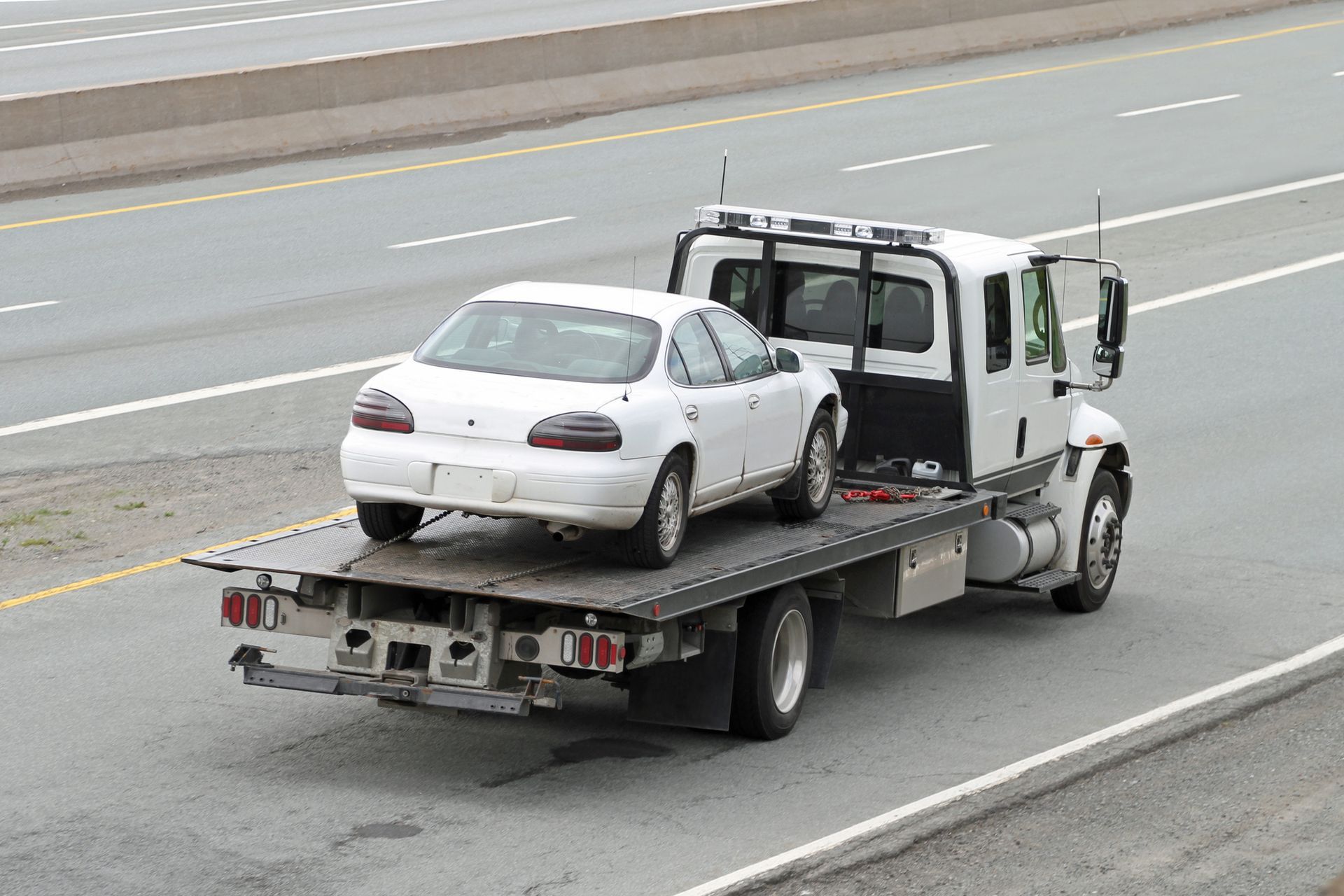 White tow truck carrying a white sedan on a highway.