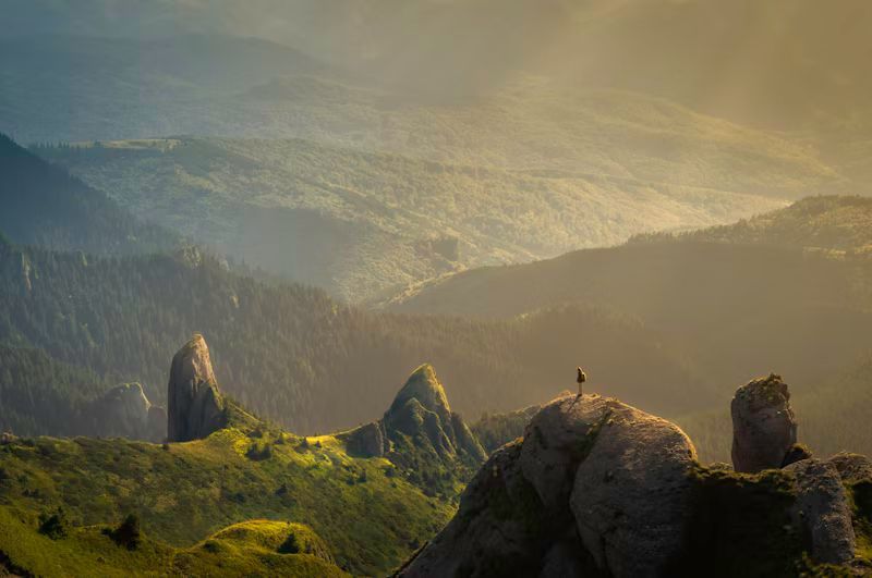 A person is standing on top of a rock in the mountains.