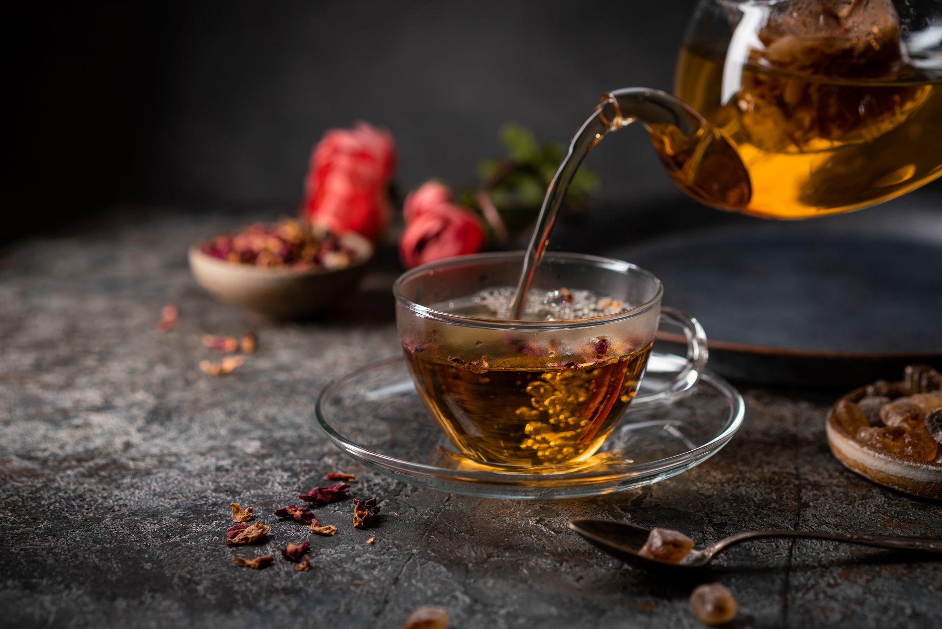Tea being poured from a glass teapot into a glass teacup on a saucer. Tea being poured from a glass teapot into a glass teacup on a saucer.