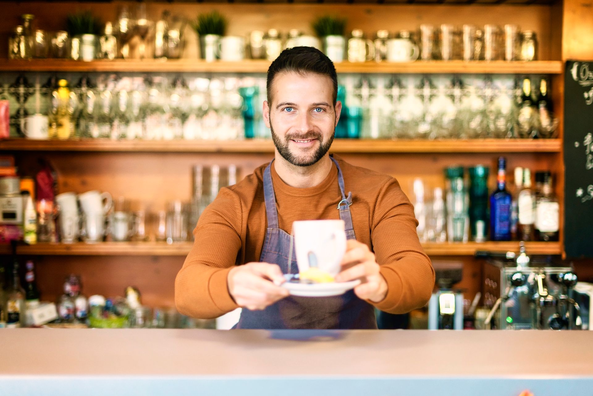 Smiling male teahouse owner standing behind the counter and offering a hot tea.