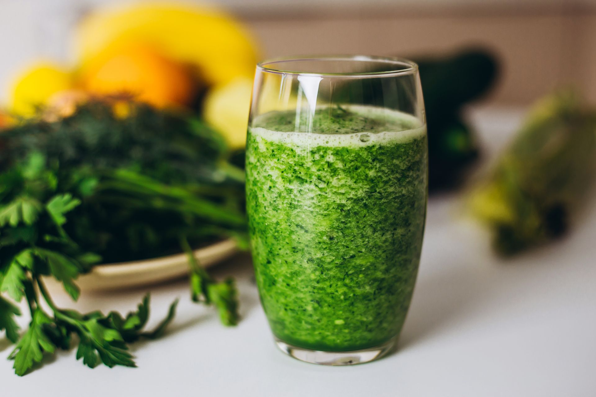 Green smoothie in a glass, surrounded by fresh herbs and fruit.